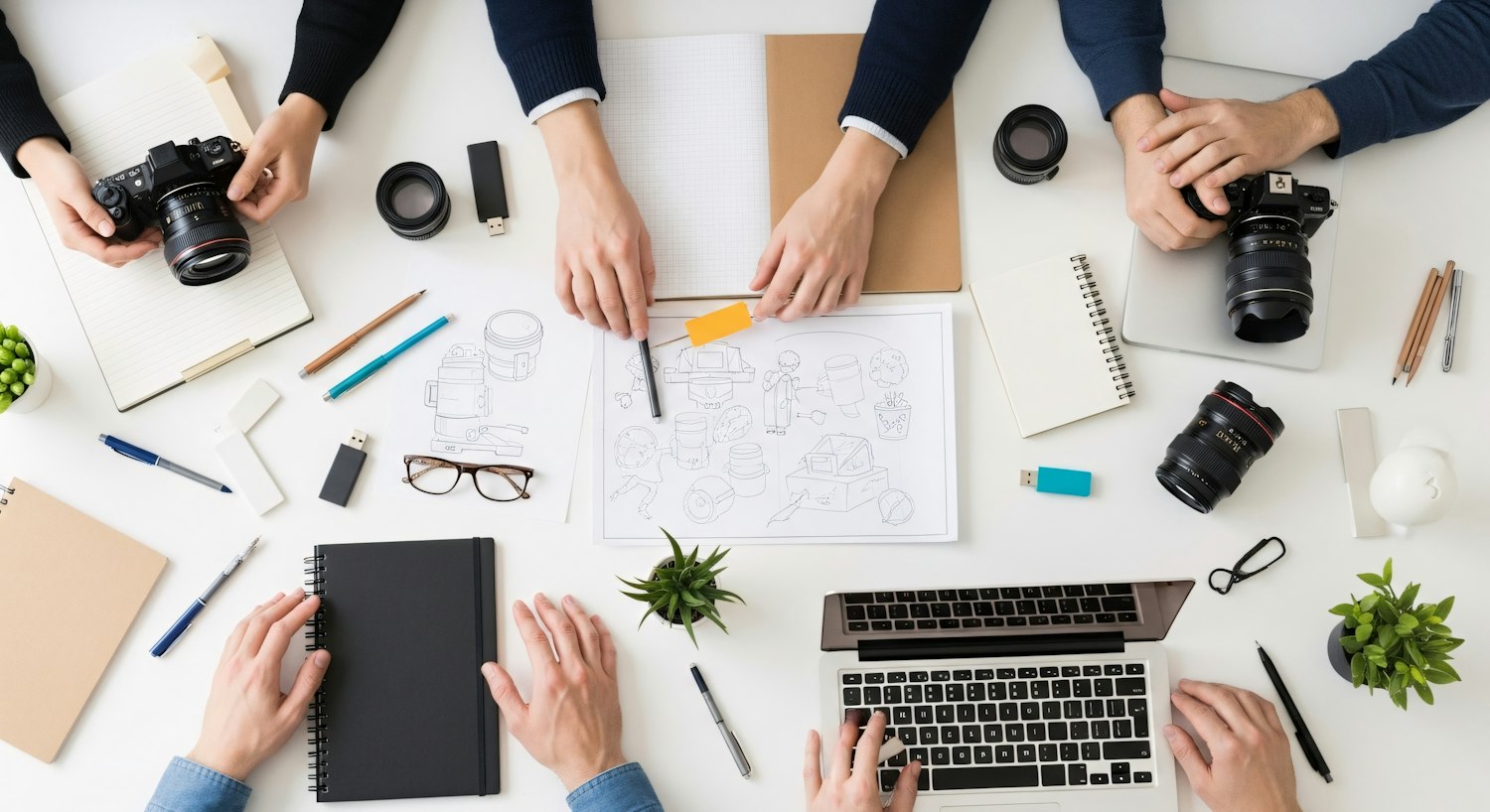 A creative team working around a table with cameras, sketches and a laptop