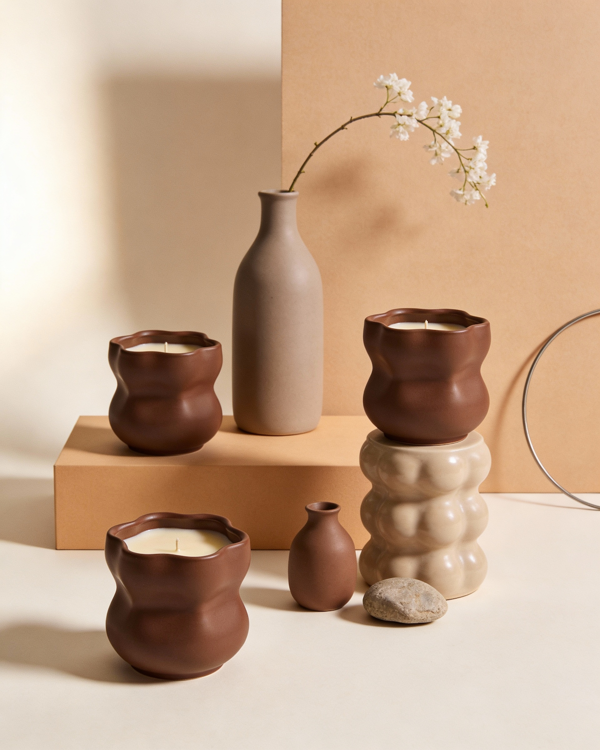 Handmade brown ceramic candles and vases arranged on warm beige plinths